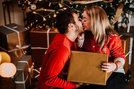 Perfect couple wearing red sweaters, kissing and opening santa presents on Christmas morningの写真素材