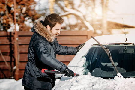 Transportation, vehicles, winter, people concept - man cleaning car from snow during cold sunny day