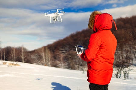 Portrait of man with red winter jacket flying drone, operating uav hobby aircraft