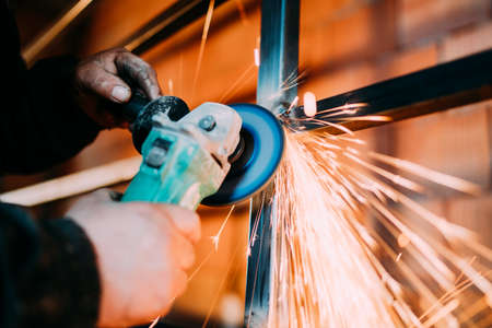 Metalworker using disc grinder for cutting metal in construction industry
