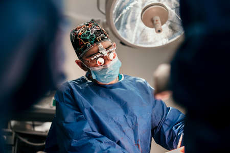 Surgeon doctor and team of doctors performing operation on live patient in sterile hospital roomの写真素材
