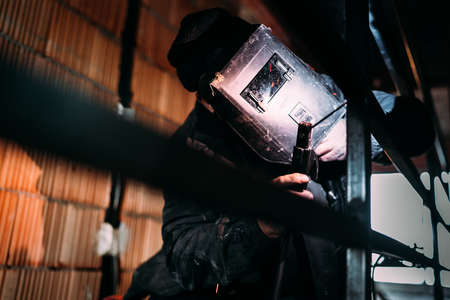 Professional construction worker with protective mask welding metal