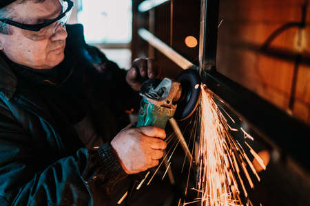 industrial male worker using angle grinder for cutting indoor metal railings