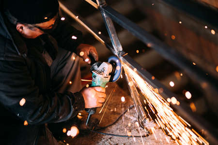 Metalworker cutting iron and metal with a rotary angle grinder and working, generating metal sparks