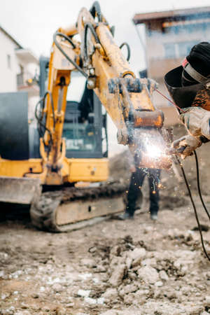 Close up details of professional welder working on broken excavator, repairing and working