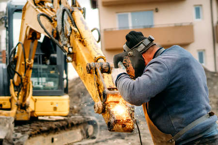 Close up portrait of welder working on excavator on construction site, reparing and fixingの写真素材