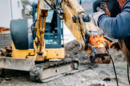 Professional worker welding excavator arm on construction siteの写真素材