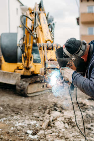 Professional welder with protection gear and mask welding broken excavator armの写真素材