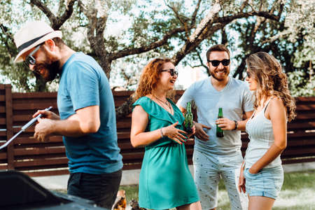 Friends having a barbecue party and girls laughing and drinking light beers on a hot summer day