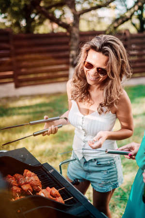 Young attractive woman smiling and cooking at barbecue grill party. Friends, people lifestyle conceptの写真素材