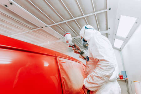 automotive industry details - close up of painter applying red paint on a red car wearing protective clothingの写真素材