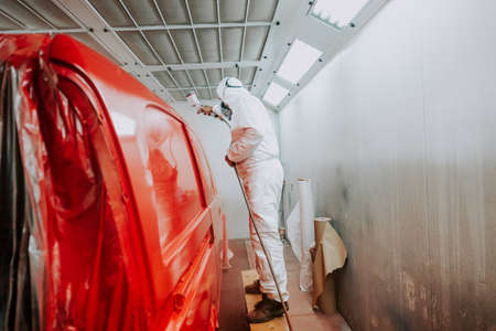 worker painting a red car in a special garage, wearing a white costumeの写真素材