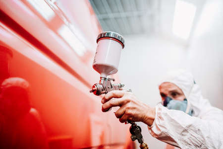 close up of worker painting a red car in a special garage, wearing a white costumeの写真素材