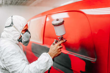 worker painting a car in a special painting box, wearing a white costume and a breathing helmetの写真素材