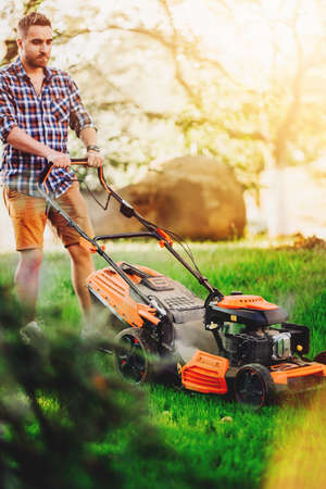 Portrait of handsome gardenere worker using lawnmower and cutting the garden grass
