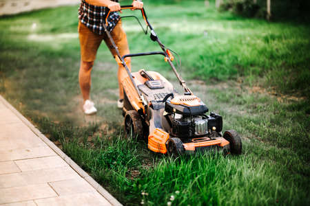 Gardening and landscaping concept - worker, gardener working with lawnmower and cutting grass in gardenの写真素材