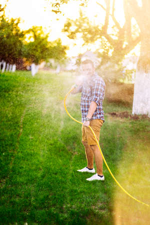 Garden maintainance- man playing with hose and watering the lawnの写真素材