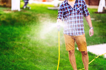 Gardener working in garden, using hose and watering plantsの写真素材