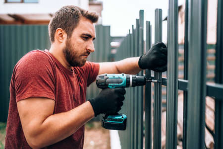Handyman worker working at outdoor metal fence on new house construction siteの写真素材
