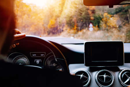 Portrait of caucasian driver holding hands on steering wheel and driving during sunset hourの写真素材