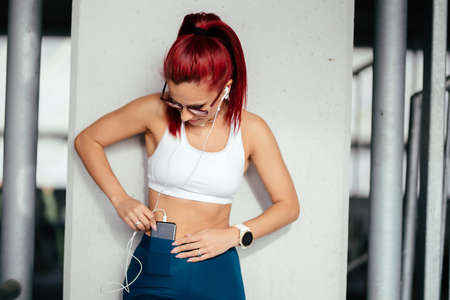 Beautiful young sportswoman in sportswear listening to music using a phone and smiling
