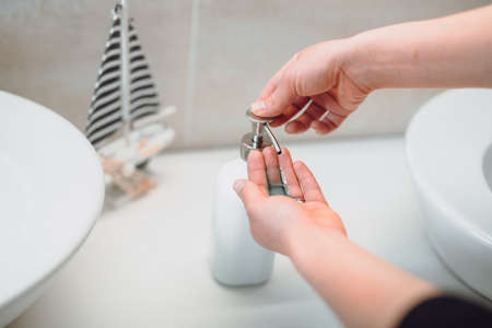 Woman using soap dispenser and washing hands at home