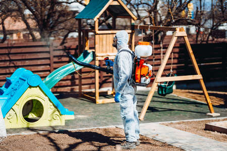 Coronavirus quarantine. Caucasian man wearing protective hazmat suit spraying disinfectant and chemicals. Protection and prevention amid coronavirus pandemicの写真素材