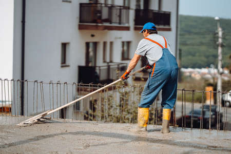 Mason building using a wooden trowel and leveling a first layer of fresh concrete floor at house, construction siteの写真素材