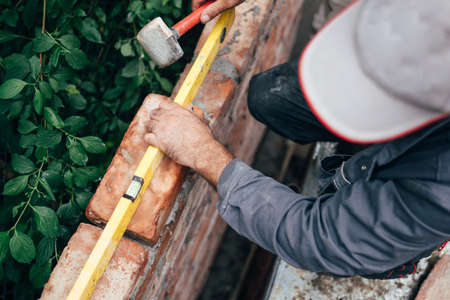professional construction worker laying bricks and building brick walls in industrial site. Detail...