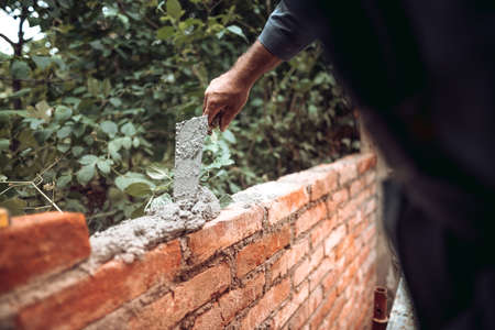 Worker placing and installing bricks on exterior wall on house construction. Worker using mortar, trowel and putty knifeの写真素材