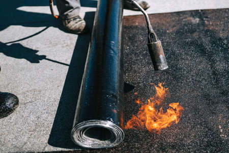 Construction workers installing bituminous membrane waterproofing system insulation using blowtorch and gasの写真素材