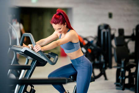 Fit active woman in the gym, working out and smiling on stationary bicycle at gym.  Fitness and bodybuilding conceptの写真素材