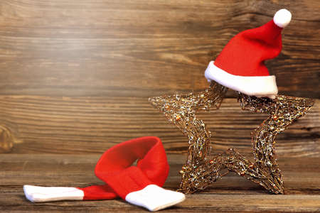christmas star close up in a santa claus hat and red scarf near by, christmas decoration on a wooden background with lightの写真素材