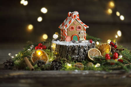 A little gingerbread house on the stump on the wooden background with lights, christmas atmosphereの写真素材