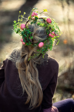 Easter wreath with weggs on a girl's head against blurred green background. spring holidays concept