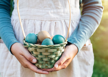 Easter rustic colored eggs in wicker basket in hands of a woman in linen cloth against blurred green background. spring holidays conceptの写真素材