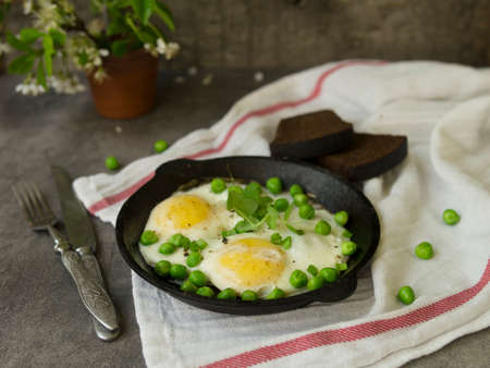 Delicious breakfast - fried eggs with green peas. On a dark background. Close up, copy spaceの写真素材