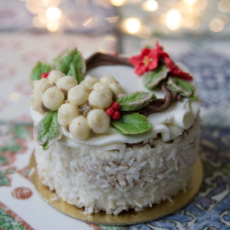 White New Year or Christmas cake decorated with cream poinsettia flowers, pine cones, cottons and spruce twigs on a colorful table. A birthday cake for those born in winter.Copy space, selective focusの写真素材