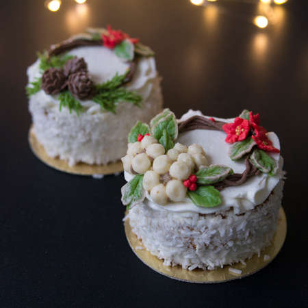 White New Year or Christmas cake decorated with cream poinsettia flowers, pine cones, cotton and spruce twigs on a black background with lights. Slice of cake. Copy space, selective focusの写真素材