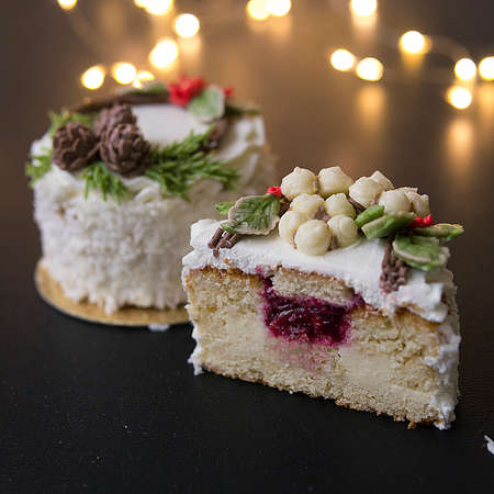 White New Year or Christmas cake decorated with cream poinsettia flowers, pine cones, cotton and spruce twigs on a black background with lights. Slice of cake. Copy space, selective focusの写真素材