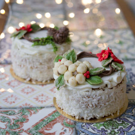 White New Year or Christmas cake decorated with cream poinsettia flowers, pine cones, cottons and spruce twigs on a colorful table. A birthday cake for those born in winter.Copy space, selective focusの写真素材