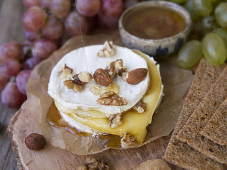 Baked Camembert on wooden board, branch of green and red grapes, rosemary, rye bread, nuts and honey. Close up, copy space, selective focusの写真素材