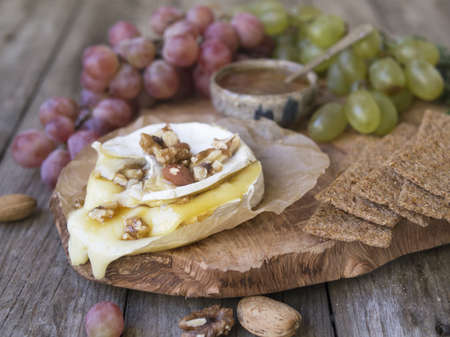Baked Camembert on wooden board, branch of green and red grapes, rosemary, rye bread, nuts and honey. Close up, copy space, selective focusの写真素材