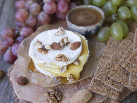 Baked Camembert on wooden board, branch of green and red grapes, rosemary, rye bread, nuts and honey. Close up, copy space, selective focusの写真素材