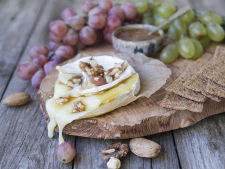 Baked Camembert on wooden board, branch of green and red grapes, rosemary, rye bread, nuts and honey. Close up, copy space, selective focusの写真素材