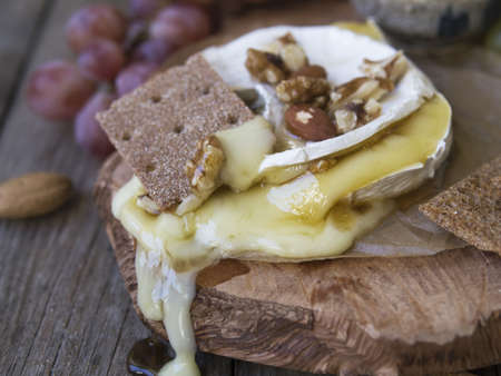 Baked Camembert on wooden board, branch of green and red grapes, rosemary, rye bread, nuts and honey. Close up, copy space, selective focusの写真素材