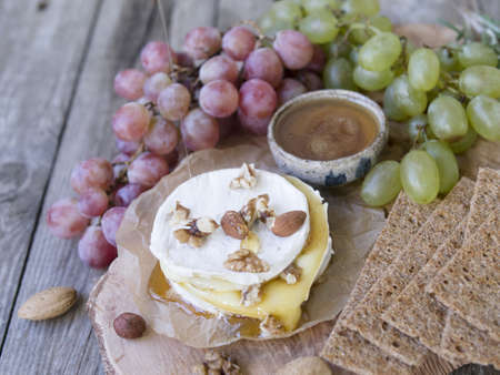 Baked Camembert on wooden board, branch of green and red grapes, rosemary, rye bread, nuts and honey. Close up, copy space, selective focusの写真素材