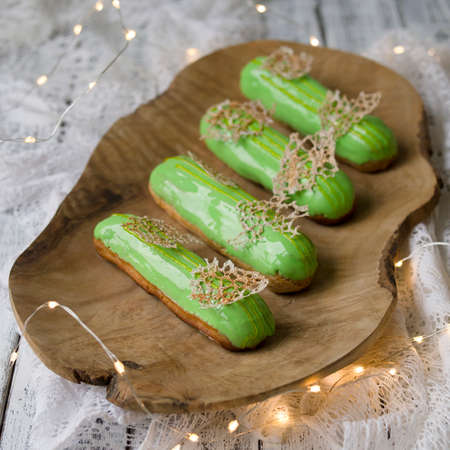 Eclairs with tangerine jelly, orange mousse and mascarpone cream decorated with green icing and gold lace decoration on wooden plate. The concept of Christmas and New Year. Closeup, selective focusの写真素材