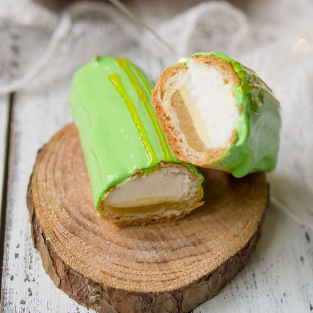 Eclair cut with tangerine jelly, orange mousse and mascarpone cream decorated with green icing and gold lace decoration on wooden plate. The concept of Christmas and New Year.Closeup, selective focusの写真素材