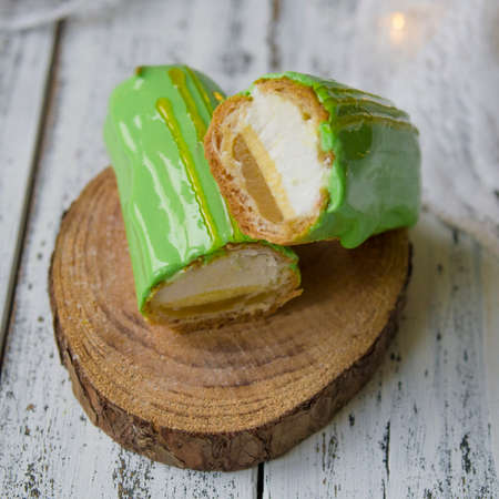Eclair cut with tangerine jelly, orange mousse and mascarpone cream decorated with green icing and gold lace decoration on wooden plate. The concept of Christmas and New Year.Closeup, selective focusの写真素材